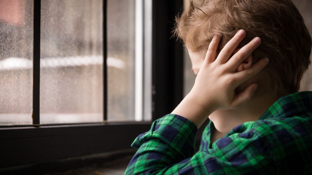 Petit garçon devant fenêtre les mains sur les oreilles